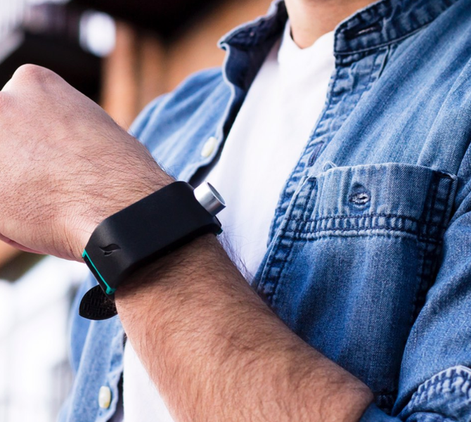 Der Oberkörper eines Mannes ist abgebildet. Er hält seine linke Hand hoch, an dem er das Sunu Band befestigt hat.