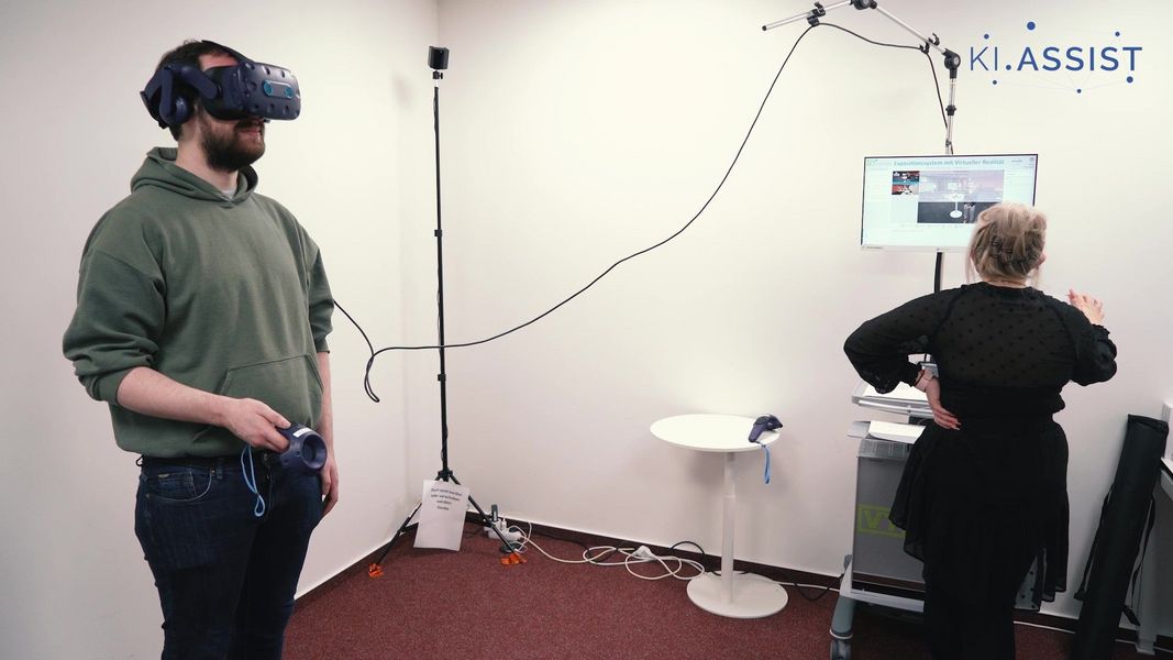 Rene mit dem KI-gestützten Assistenzsystem OPTAPEB. Zusätzlich steht eine Frau an einem Computer, der anzeigt, was Rene durch die VR Brille sieht