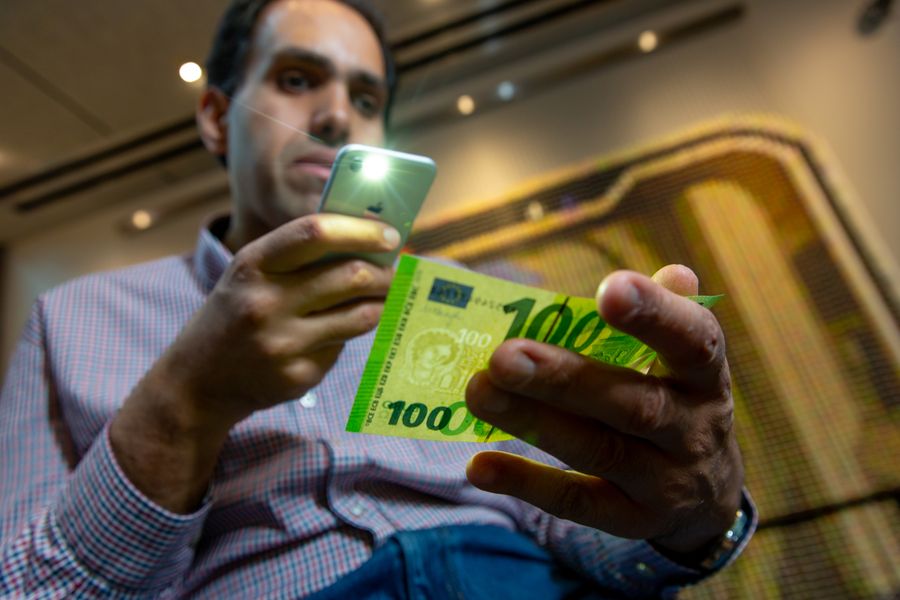 Mann hält ein Smartphone in der Hand. Er scannt einen grünen Geldschein.