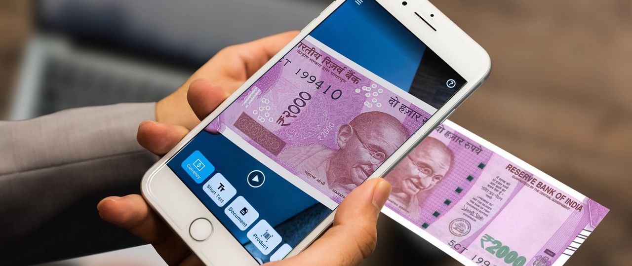 Person hält ein Smartphone in der Hand. Person scannt einen Geldschein.