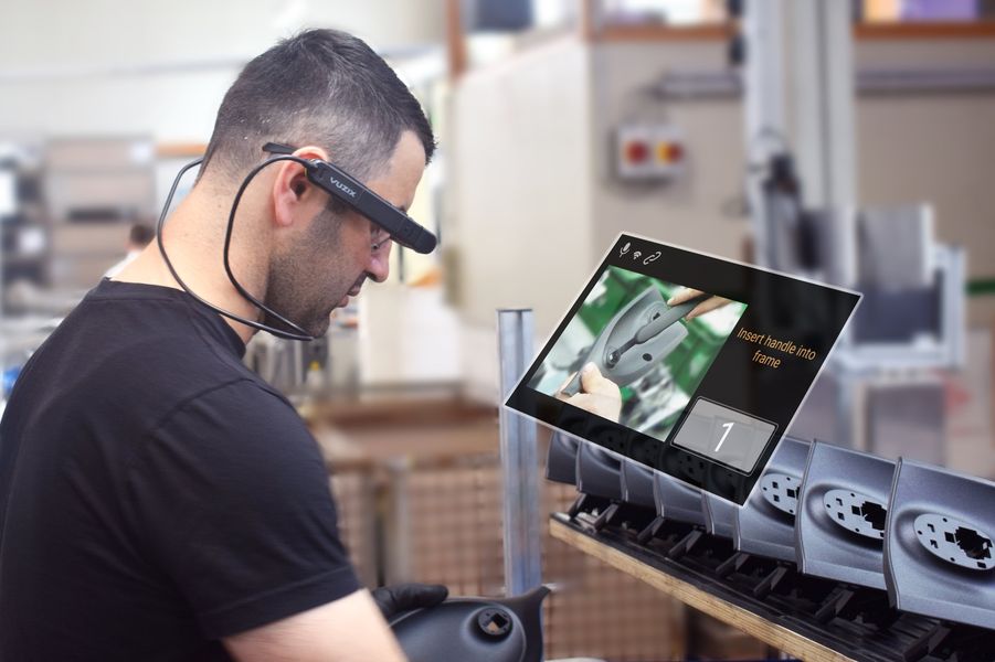 Ein Mann ist von der Seite zu sehen. Er steht vor einem artifiziellen Bildschirm und hat eine Datenbrille an.