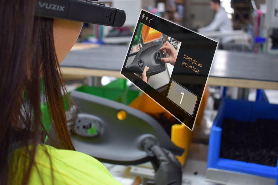 Eine Person ist setilich von hinten zu sehen. Sie trägt eine Datenbrille und guckt auf einen artifiziellen Bildschirm, der einen Vorgangsschritt anzeigt