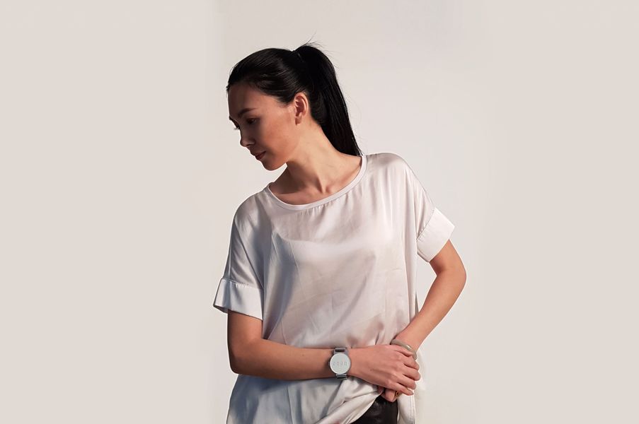 Eine Frau mit einem weißen Oberteil ist abgebildet. Sie fasst sich an die Hüfte und trägt an ihrem Handgelenk die Dot Watch.