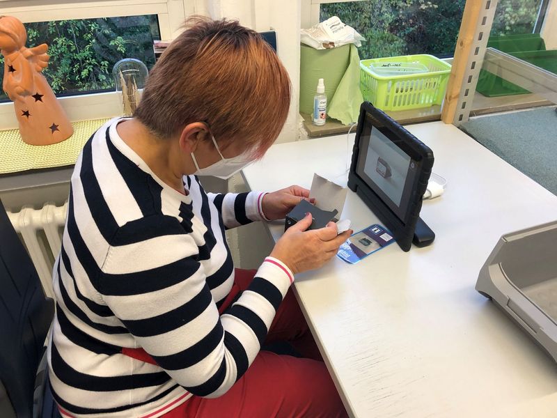 Eine Frau sitzt am Schreibtisch und hat ein Tablet vor sich und eine Verpackung in der Hand.
