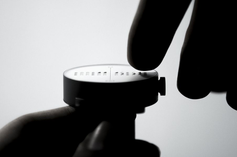 Eine schwarz-weiß Aufnahme zeigt einen Finger, der die Uhrzeit auf der Dot Watch abliest.