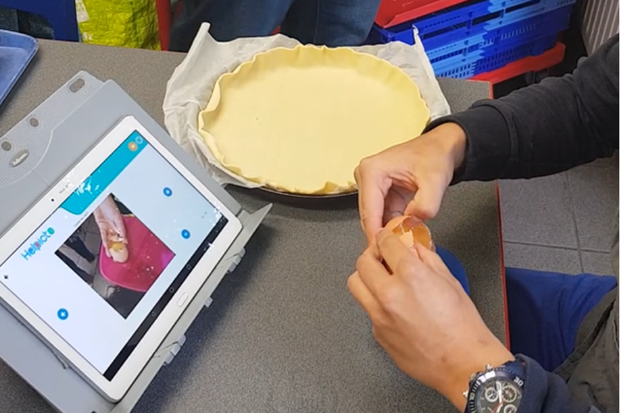 Zwei Hände teilen ein Ei. Die Helpicto-App ist auf dem Tablett geöffnet.