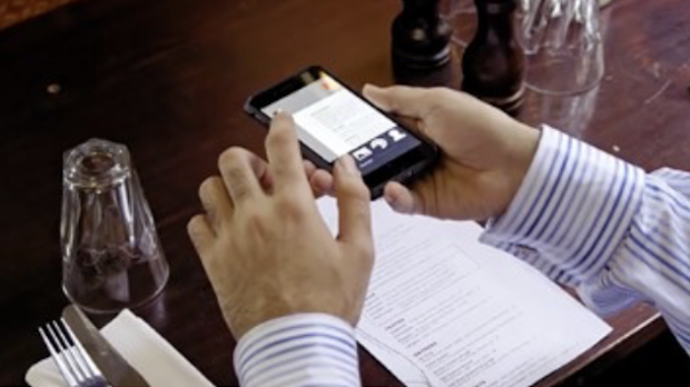 Hände halten ein Smartphone mit der App über eine Speisekarte.