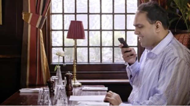 Ein Mann sitzt im Restaurant und schaut auf ein Smartphone.