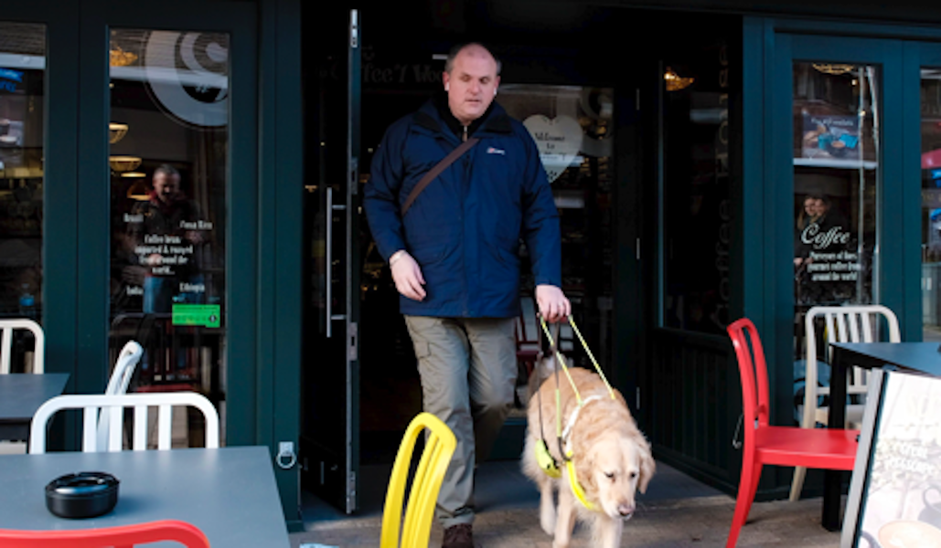 Ein Mann verlässt ein Cafe mit einem Blindenhund