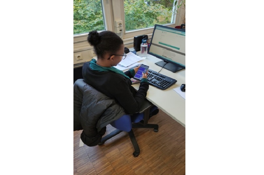 Eine Frau sitzt am Schreibtisch und guckt auf ihr Smartphone