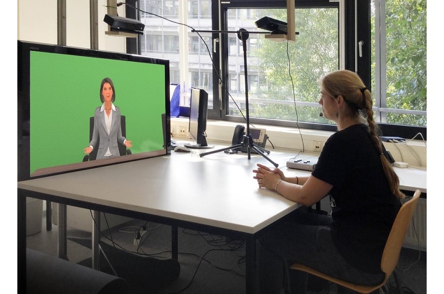 Frau sitzt vor einem Bildschirm auf dem ein Avatar abgebildet ist